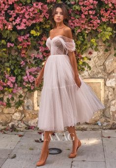 a woman standing in front of flowers wearing a white dress with sheer shoulders and an off the shoulder neckline