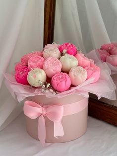 a pink and white flower arrangement in a round box on a table next to a mirror