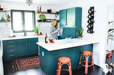 a woman standing in a kitchen next to two stools and a counter with bottles on it