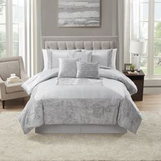 a bed with white and grey comforters in a living room next to a chair