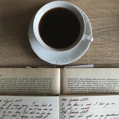 an open book next to a cup of coffee on top of a wooden table with writing