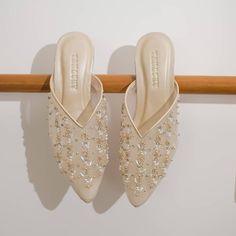 a pair of white shoes hanging on a wooden rail with beaded detailing and pearls