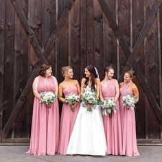 a group of women standing next to each other in front of a wooden door holding bouquets