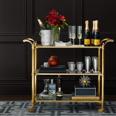 a gold bar cart filled with bottles and glasses on top of a carpeted floor