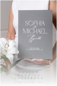 a woman holding a gray wedding book with white flowers in front of her and the words sophia and michael on it