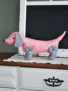 a pink and white dachshund dog sitting on top of a dresser