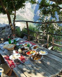 an outdoor table with plates of food and drinks on it, overlooking the valley below