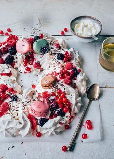 a cake decorated with berries, whipped cream and macaroni shells on a cutting board