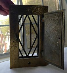 an open metal box sitting on top of a white table next to a window with a person reaching for it