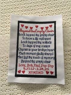 a cross stitched on top of a piece of cloth with words written in red and black