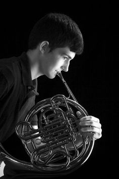 a young man holding a french horn in his right hand and looking down at it