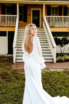 a woman standing in front of a house wearing a long white dress with ruffled sleeves