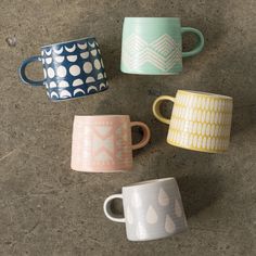 four different colored coffee mugs sitting next to each other on a cement surface,