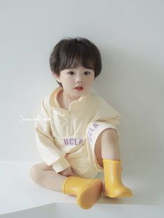 a young child sitting on the ground wearing yellow boots and a sweatshirt with words written on it