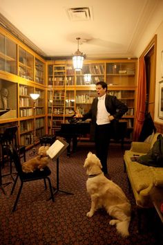 a man standing next to a dog in a living room filled with furniture and bookshelves