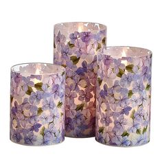 three glass candles with purple flowers on them and one candle in the middle is lit