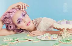 a woman with pink hair laying on a table next to some cookies and other desserts