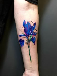 a blue flower tattoo on the left inner arm and leg, with watercolor splashes