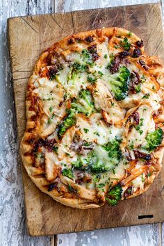 a pizza topped with broccoli and cheese on top of a wooden cutting board