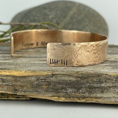 a close up of a metal bracelet on a wooden surface with a rock in the background