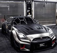 a black and silver sports car parked in front of a garage