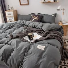 an unmade bed with grey comforter and pillows on the floor next to a window