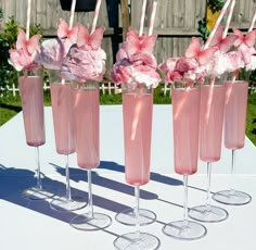 four glasses filled with pink liquid and flowers on top of a white tablecloth covered table