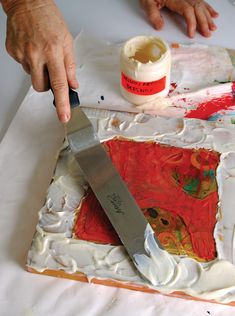 a person is using a knife to cut into a painting with white and red paint