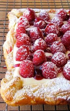 a pastry with powdered sugar and raspberries on it sitting on a cooling rack