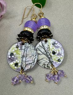 Handmade enameled charms by an Etsy artisan.  Charms are topped with black double row floral bead caps, lava rock, rhinestone spacers, hand made lavender ribbed lampwork beads, and small gold spacers. three lavender Swarovski crystals dangle from the bottom. Earrings hang 3.25 inches from the top of the ear wire. Lampwork Earring, Gilbert Az, Lava Rock, Copper Earrings, Earrings Boho, Bead Caps, Lampwork Beads, Ear Wire