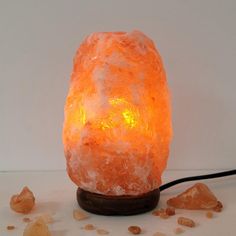 an orange himalayan salt lamp on a wooden base with rocks around it and a black cord