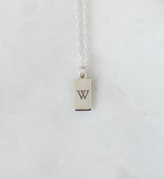 "Personalized 925 Sterling Silver Mini Tag Necklace from our Memoirs Made Collection. A lovely display of your initials, or even a short word makes for a captivating look with our stylish tag pendant necklace. NECKLACE DETAILS ⚬ Sterling silver rectangle tag and chain ⚬ Chain in your choice of 16\", 18\", or 20\" length ⚬ Rectangle measures 13.5mm x 6mm (.53\" x .23\") ⚬ Personalized engraving of 1-2 characters (including spaces) ⚬ Choice of 3 fonts for the engraving ⚬ Can be engraved on the rev Silver Engraved Initial Rectangular Necklace, Personalized Sterling Silver Necklace With Rectangular Pendant, Silver Engraved Square Pendant Initial Necklace, Rectangular Sterling Silver Necklace With Engraved Text, Sterling Silver Charm Necklace With Engraved Square Pendant, Short Words, Tag Necklace, Name Necklace, Initial Necklace