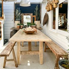 a wooden table sitting in front of a white house with potted plants on it