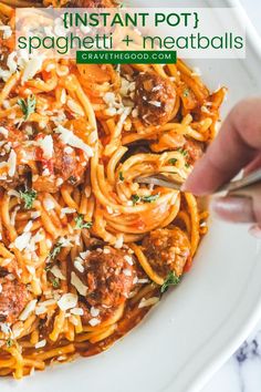 someone is eating spaghetti with meatballs and parmesan cheese in a white bowl