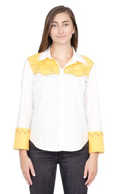 a woman wearing a white shirt with yellow details on the chest and sleeves, standing in front of a white background