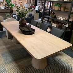 a large wooden table in a store with chairs and tables behind it, along with other furniture