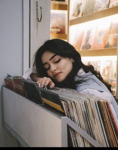 a woman leaning against a wall with her head resting on a stack of records