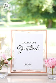 a sign that says guest book sitting on top of a table next to vases with flowers