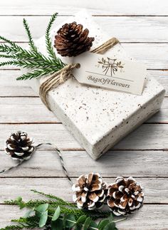 a white box with pine cones on top of it next to evergreen branches and twine