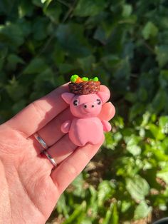 a hand holding a tiny pink pig with a crown on top of it's head