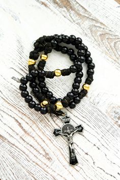 the black and gold beaded rosary bracelet is shown on a white wooden table with a cross charm