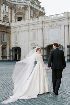 a bride and groom walking in front of an old building holding hands with each other