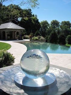 a glass ball sitting on top of a table next to a pool in the middle of a yard