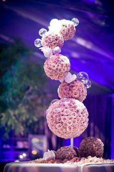 a table topped with lots of pink flowers next to a purple wall and ceiling light