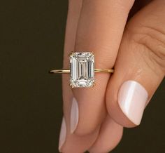 a woman's hand holding a ring with an emerald stone in the center and diamond band