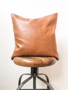 a brown leather pillow sitting on top of a metal stool