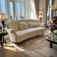 a living room filled with lots of furniture next to large window covered in white curtains