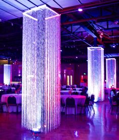 an indoor event with purple lighting and tall columns in the center, surrounded by white tablecloths