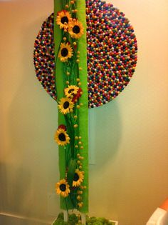 a green vase with flowers and balls on the wall in front of a circular artwork