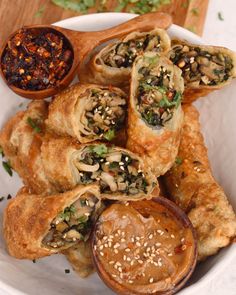 a white bowl filled with food next to a wooden spoon and some dipping sauce on the side